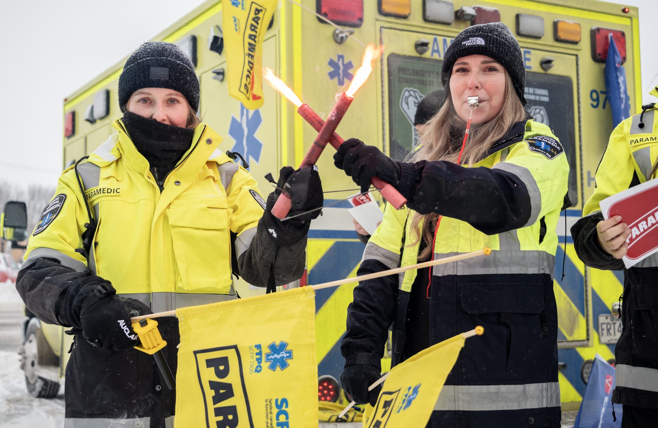 Paramédics en grève devant une ambulance, utilisant des signaux visuels pour attirer l’attention sur leur mobilisation.